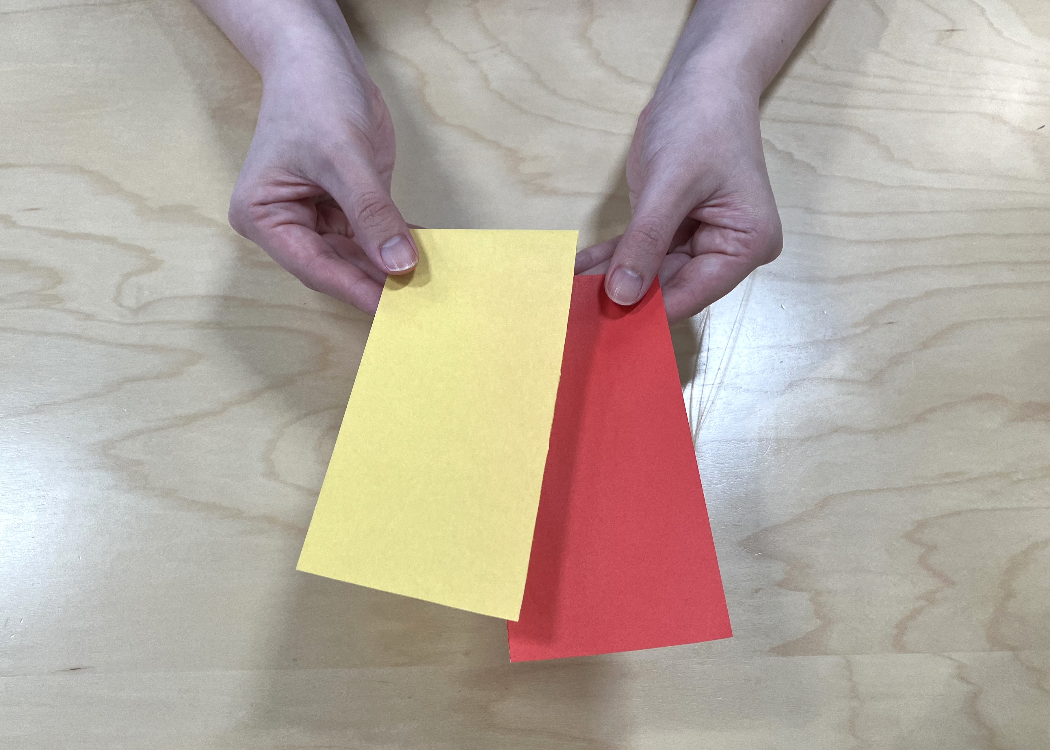 2. 半分に切った折り紙をトイレットペーパーの芯に巻き、巻き終わりをスティックのりでとめて、両端を内側に折り込みます