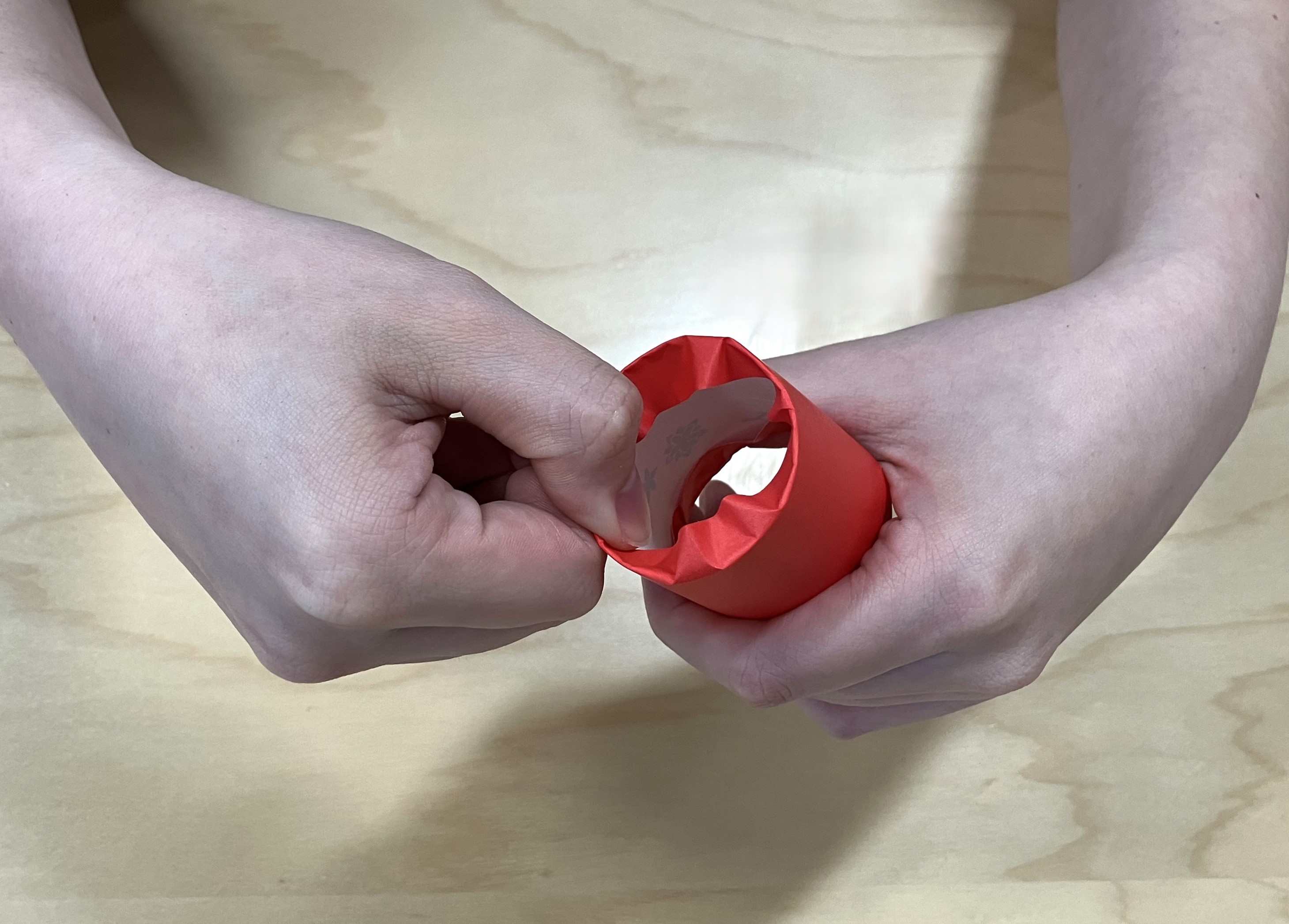 2. 半分に切った折り紙をトイレットペーパーの芯に巻き、巻き終わりをスティックのりでとめて、両端を内側に折り込みます